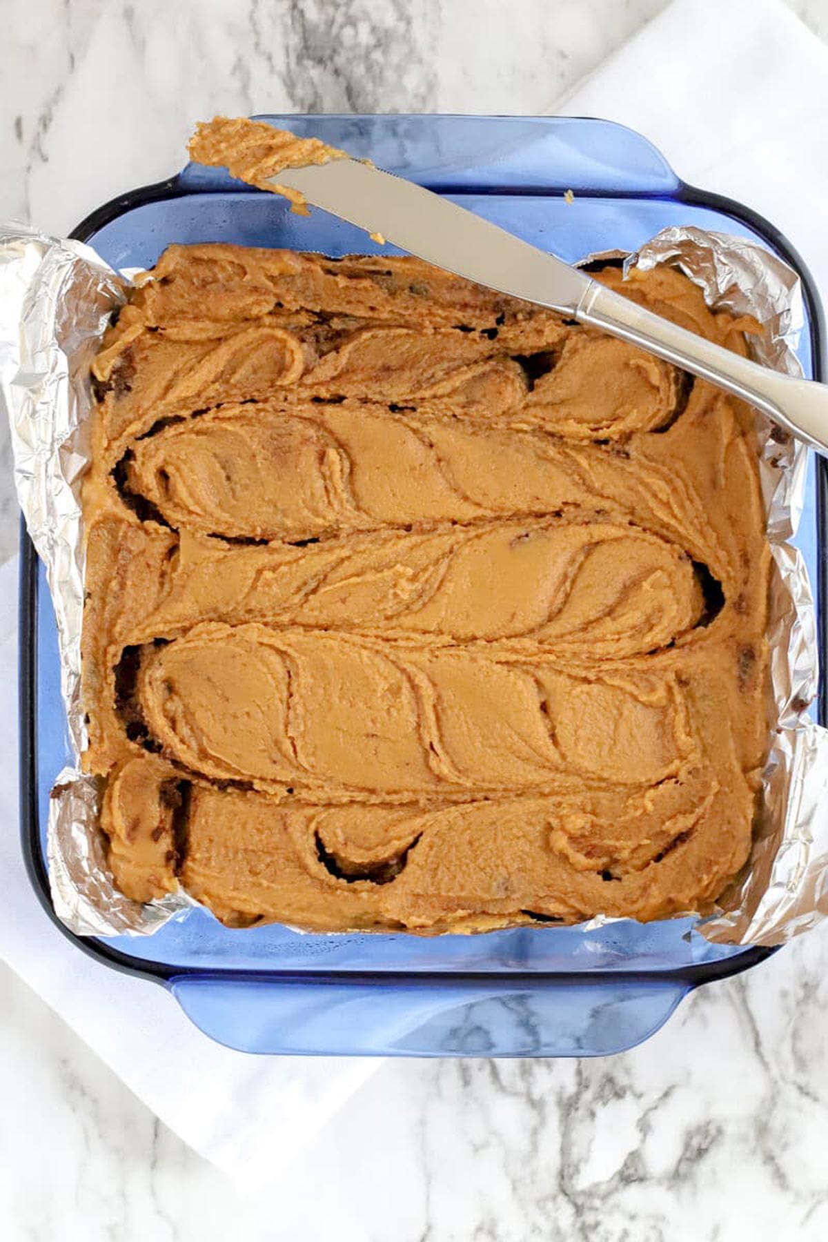 Chocolate Peanut Butter Fudge swirled with a butter knife in a blue baking dish.