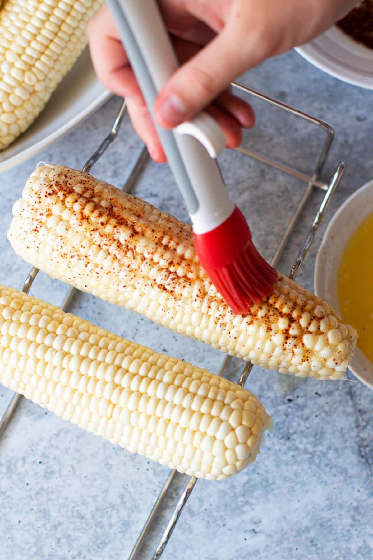 Person basting on butter to seasoned corn.