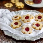 Seven linzer cookies filled with raspberry jam with sprinkled powdered sugar.