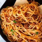 Pan containing spaghetti and meat sauce, serving spoons in pan.