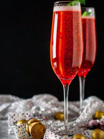 Two flutes of minted cranberry Champagne cocktail with a cork and New Year's Eve decor.