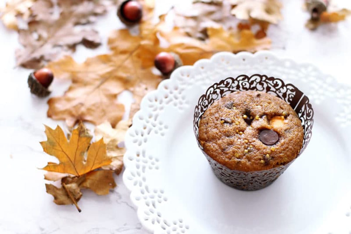 Pumpkin Chocolate Chip Muffin sitting on a white laced plate on a white table, fall leaves and acorn in background.