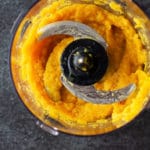 Food processor containing pureed squash on a black countertop.