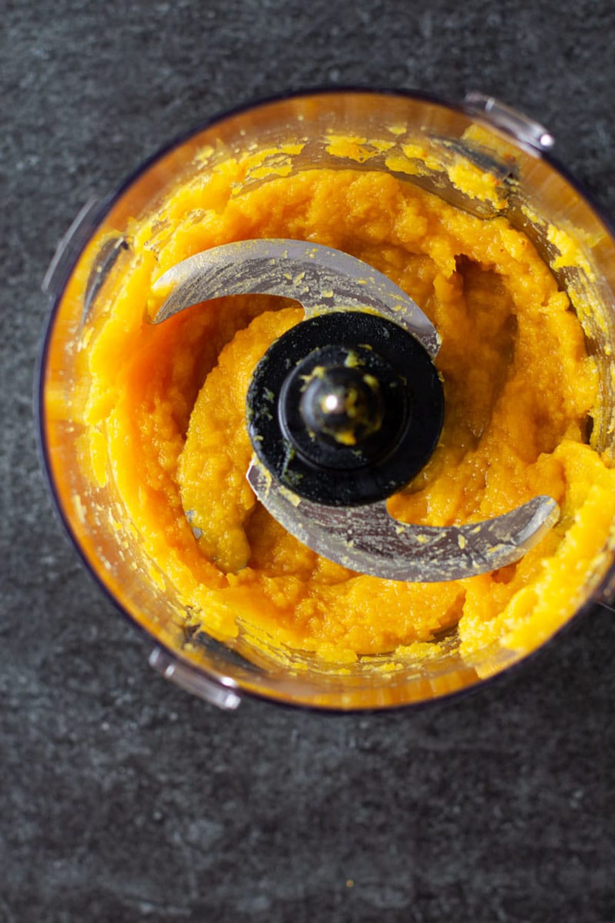 Food processor containing pureed squash on a black countertop.