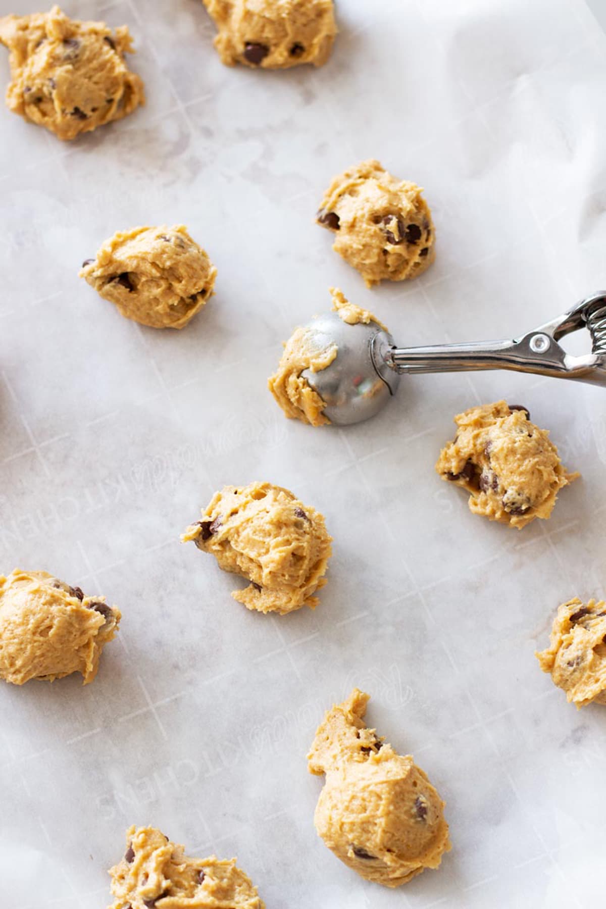 Cookie dough being placed on parchment paper lined cookie sheet with a cookie scoop.