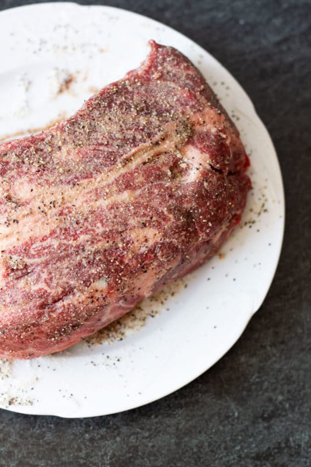 Raw chuck roast covered in a dry rub containing salt, pepper, and garlic powder.