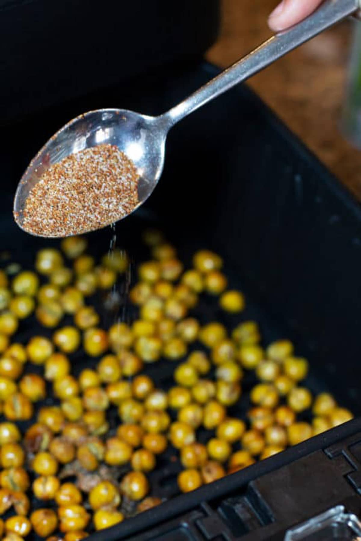 Spoonful of chili lime seasoning being poured onto chickpeas in an air fryer.