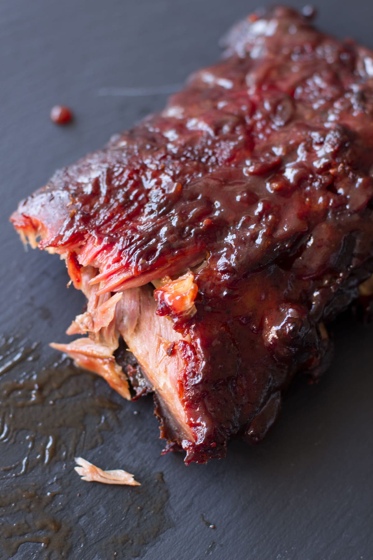 Slab of smoked BBQ Ribs on a black cutting board.