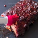 Slab of ribs being basted in BBQ sauce.