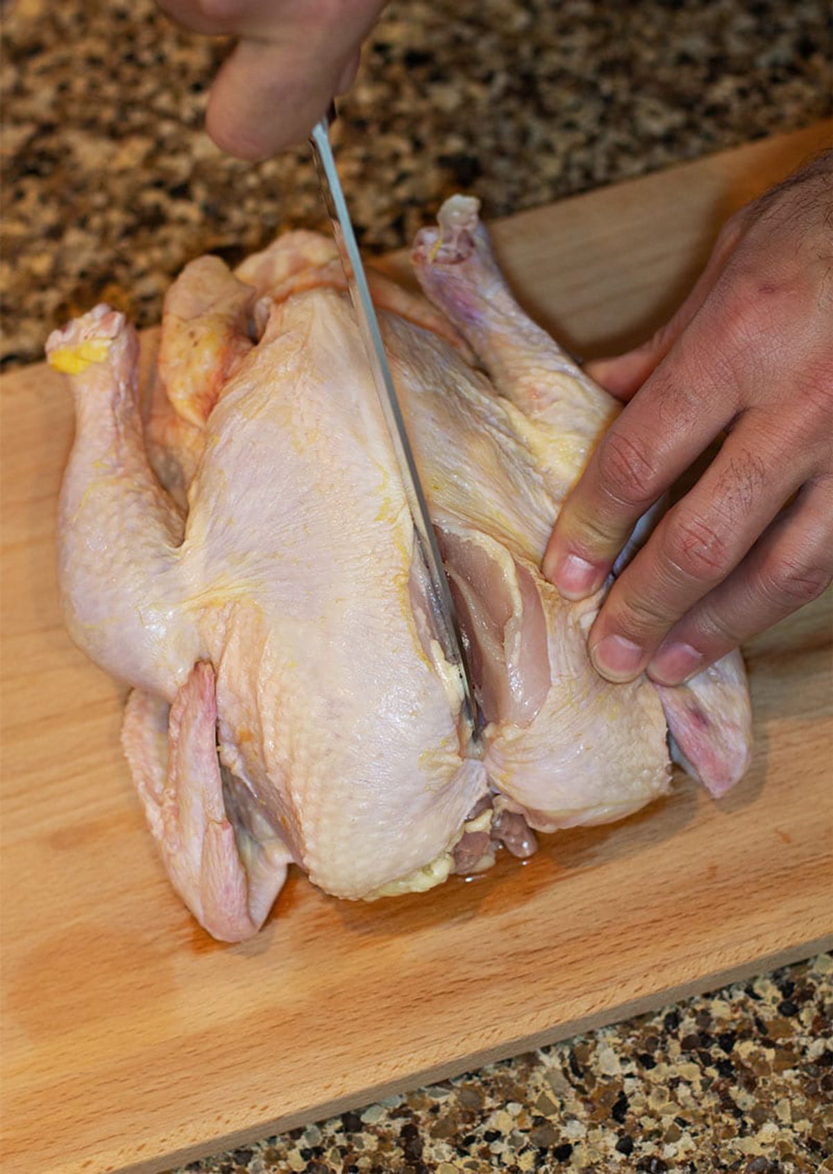 Man cutting a whole raw chicken through the breast bone. 