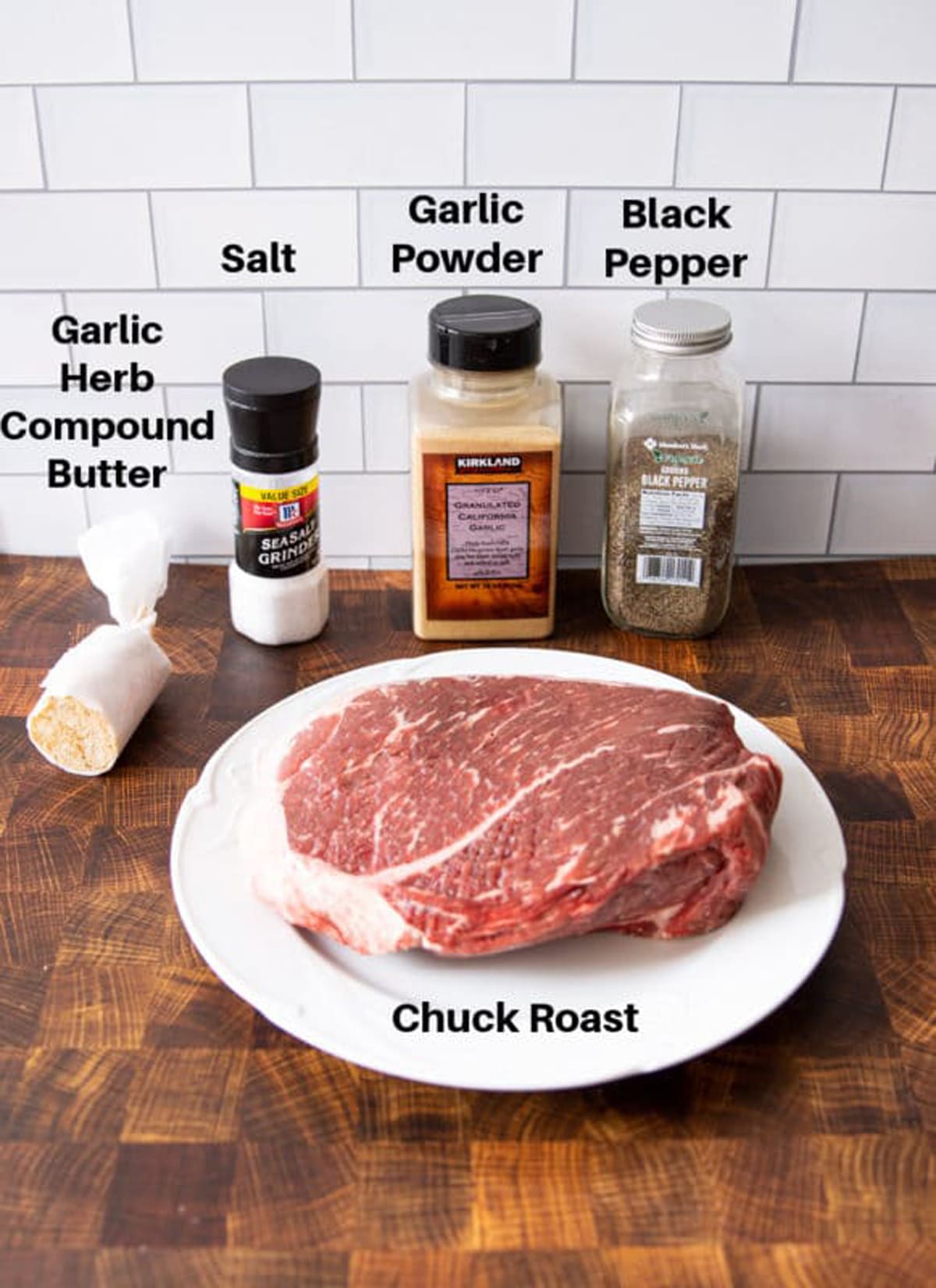 Chuck roast, salt, pepper, garlic powder, and compound butter sitting on a counter. 