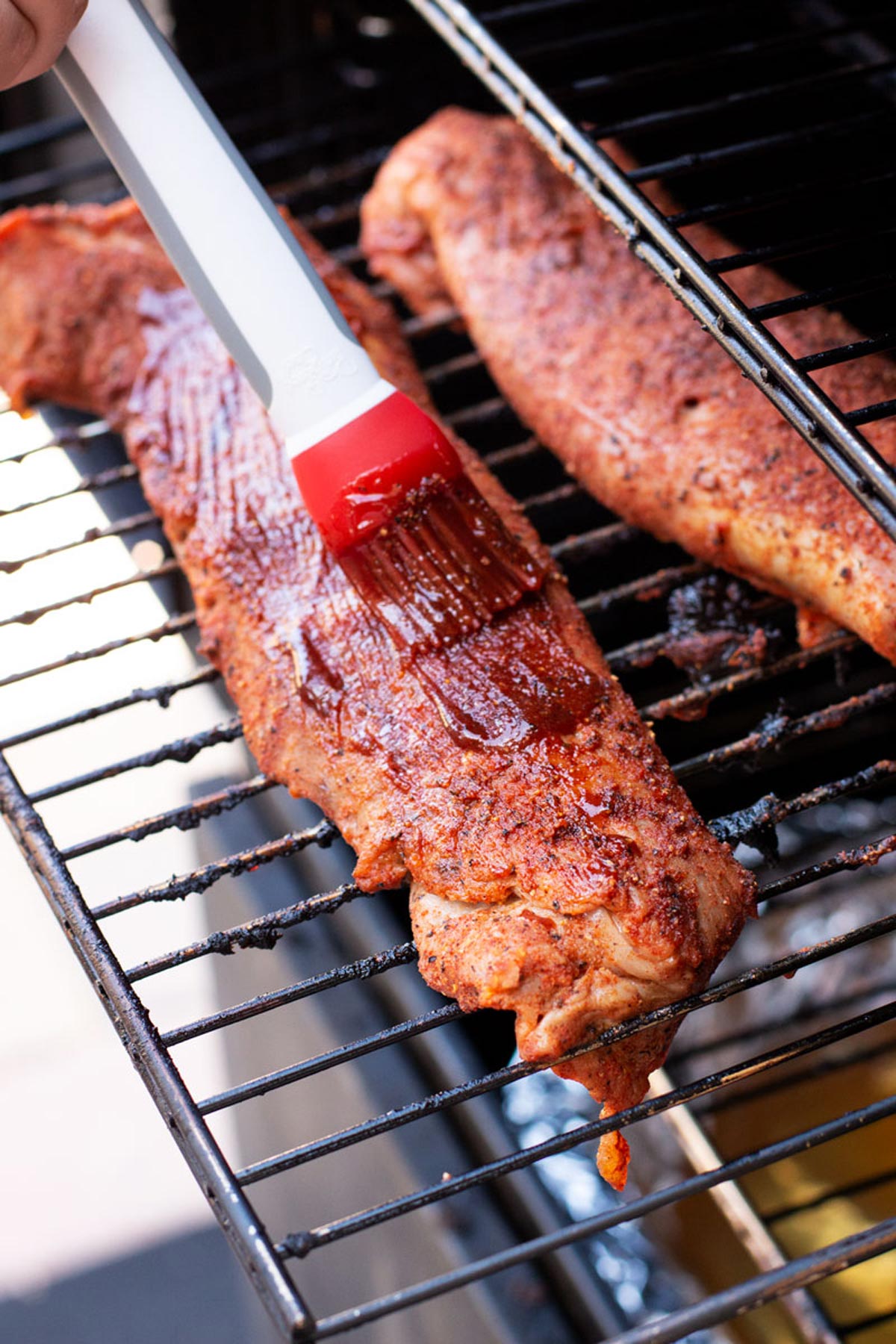 Basting brush with BBQ sauce on pork tenderloins on a smoker. 