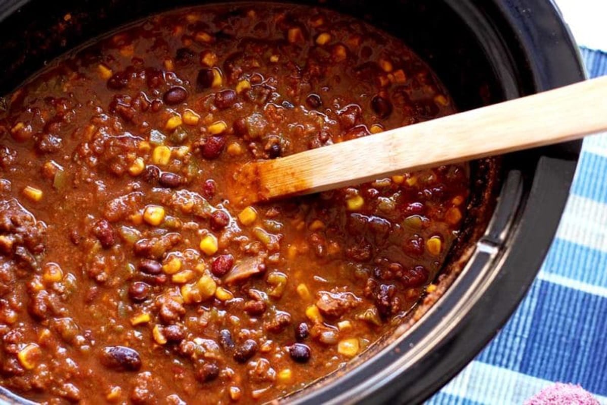 Black crock pot containing beans, corn, salsa, and peppers.