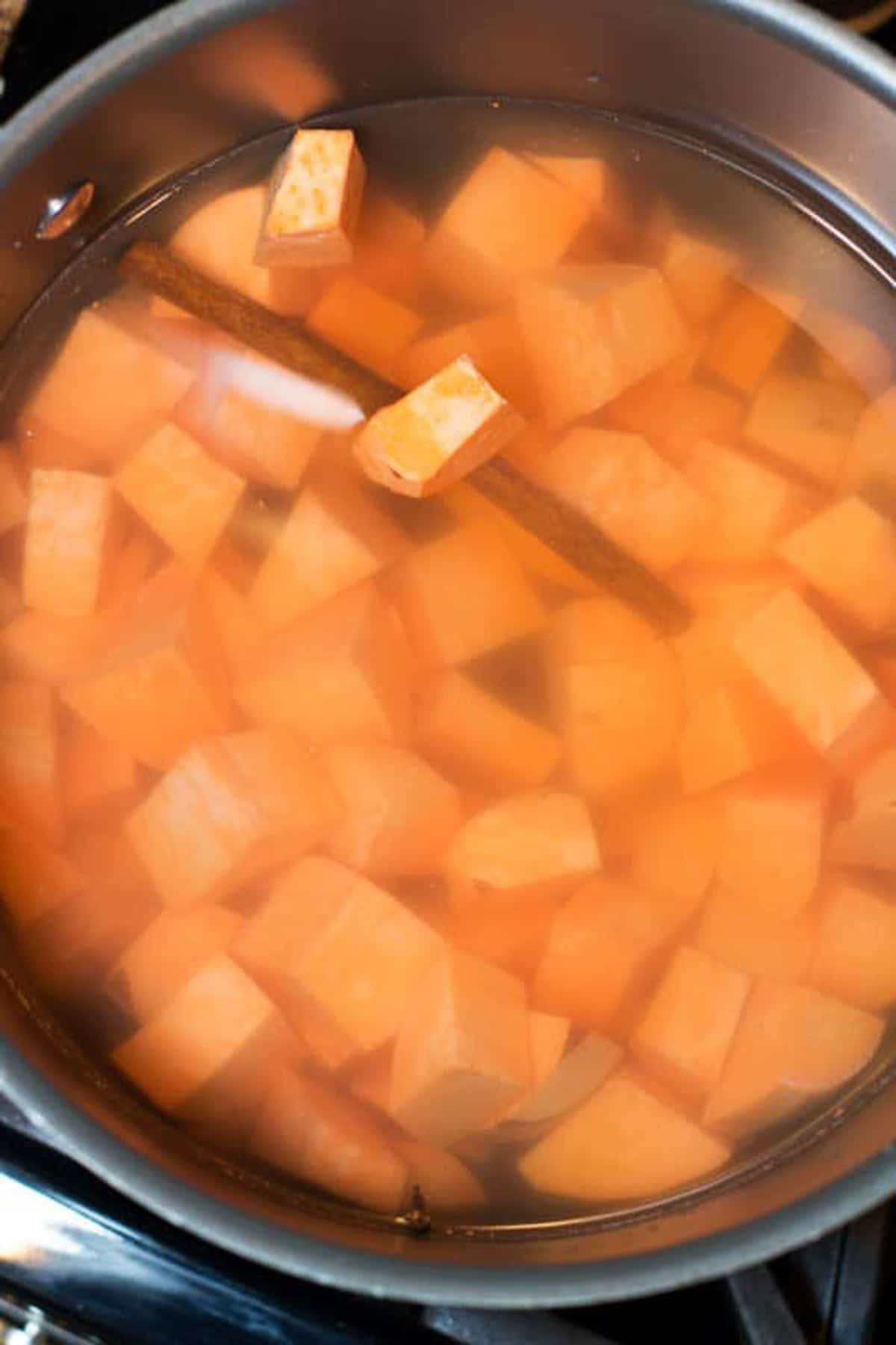Pot filled with water and chopped sweet potatoes and a cinnamon stick.