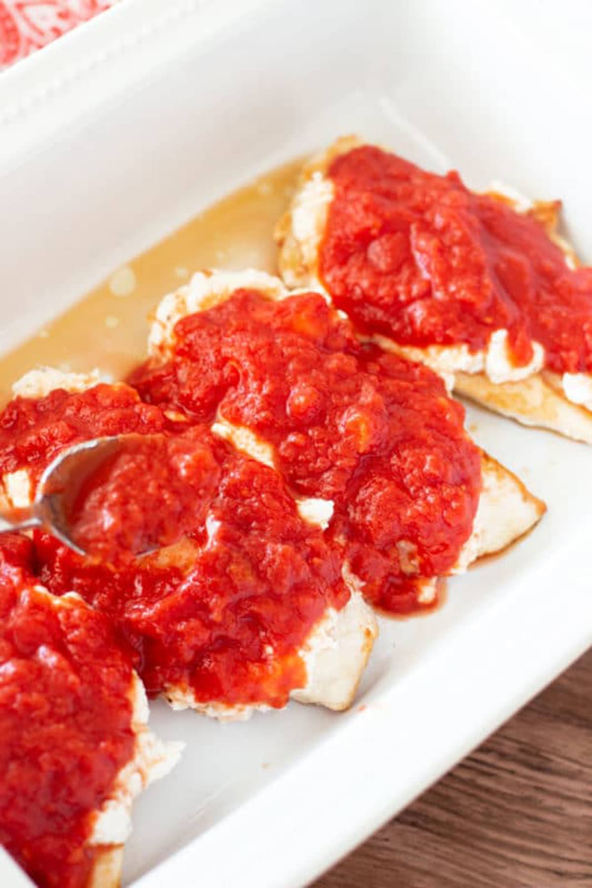 Spoonful of of crushed tomatoes topping ricotta covered chicken breasts. 