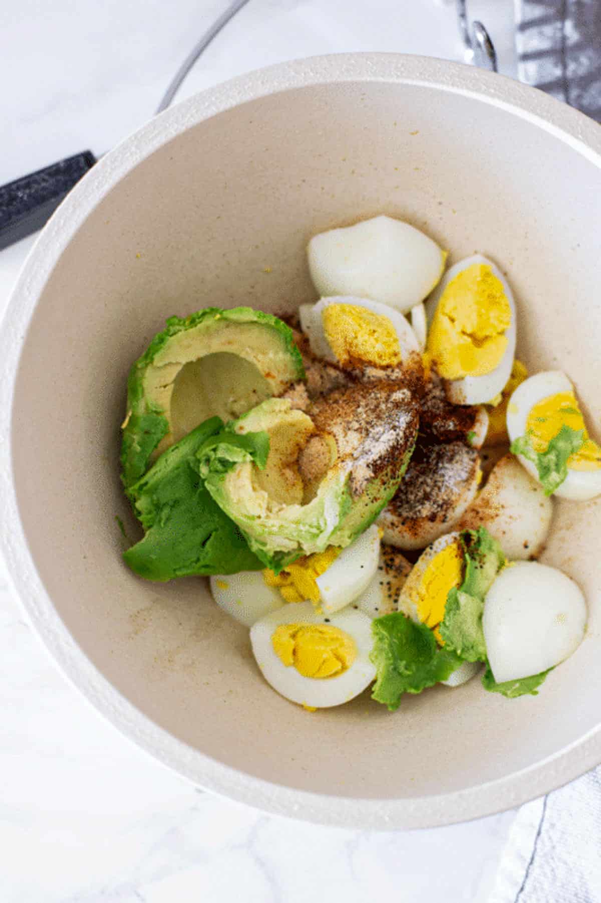 Avocado, eggs and spices in a bowl for Avocado Egg Salad.