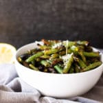 White bowl containing grilled green beans, lemon on table.
