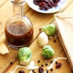Bottle of vinaigrette dressing sitting on wooden table, brussels sprouts, garlic and cranberries on table.