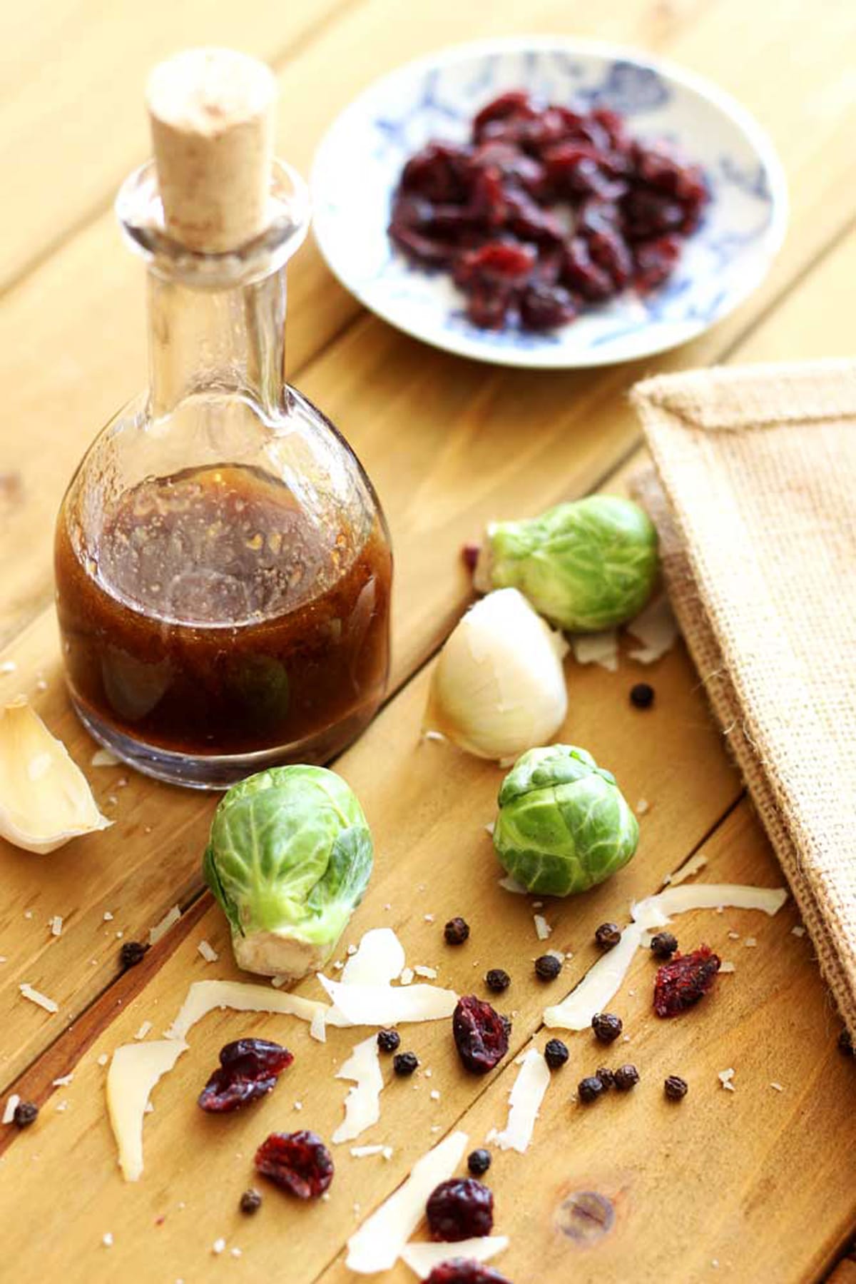 Bottle of vinaigrette dressing sitting on wooden table, brussels sprouts, garlic and cranberries on table.