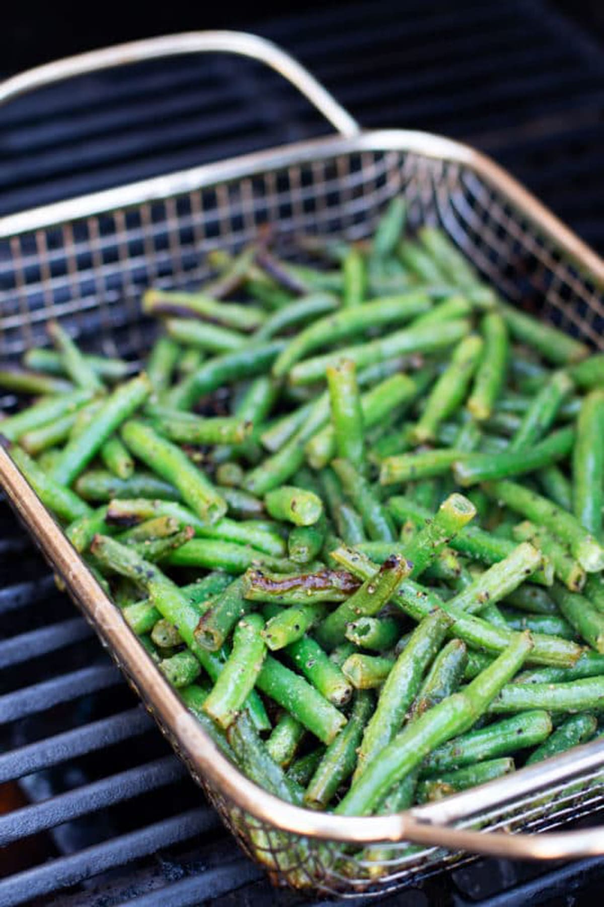 Long green beans in a grilling basket on a grill.