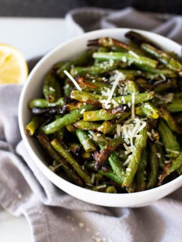 White bowl containing grilled green beans, topped with Parmesan cheese.