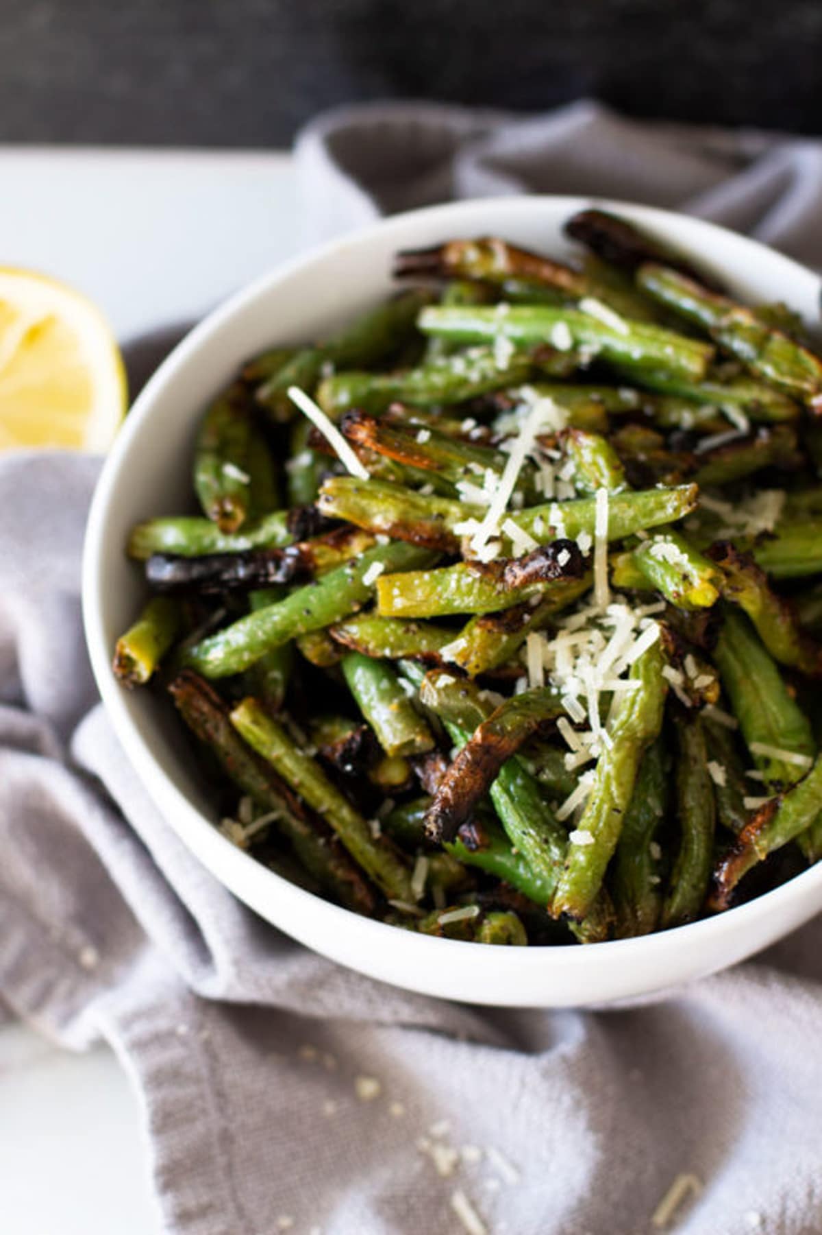 White bowl containing grilled green beans, topped with Parmesan cheese. 