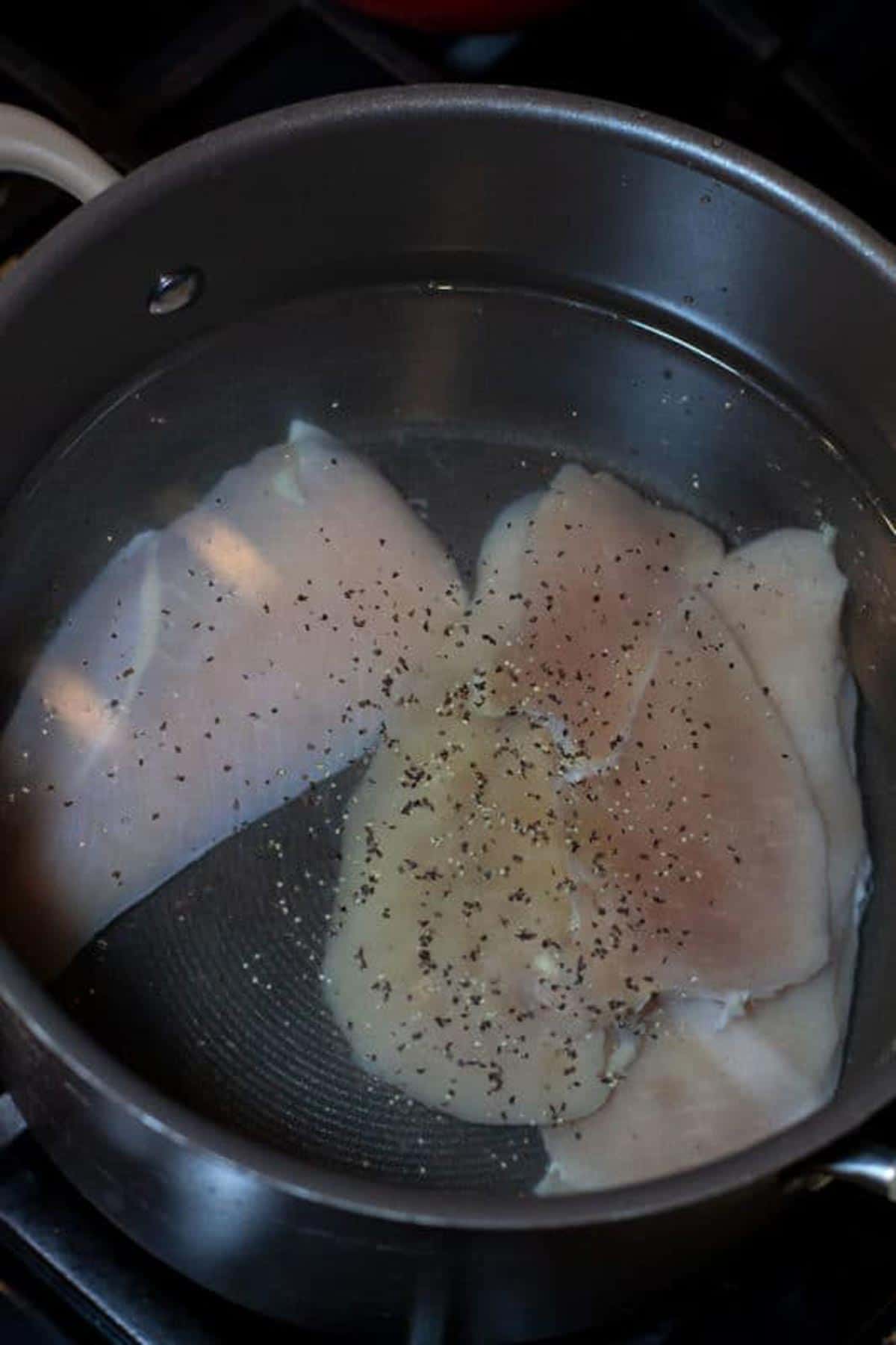 Large pot containing raw chicken being brought to a boil, pinch of salt and pepper in water.