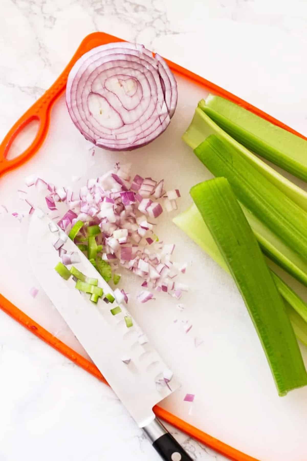 Cutting board with chopped red onion and celery.