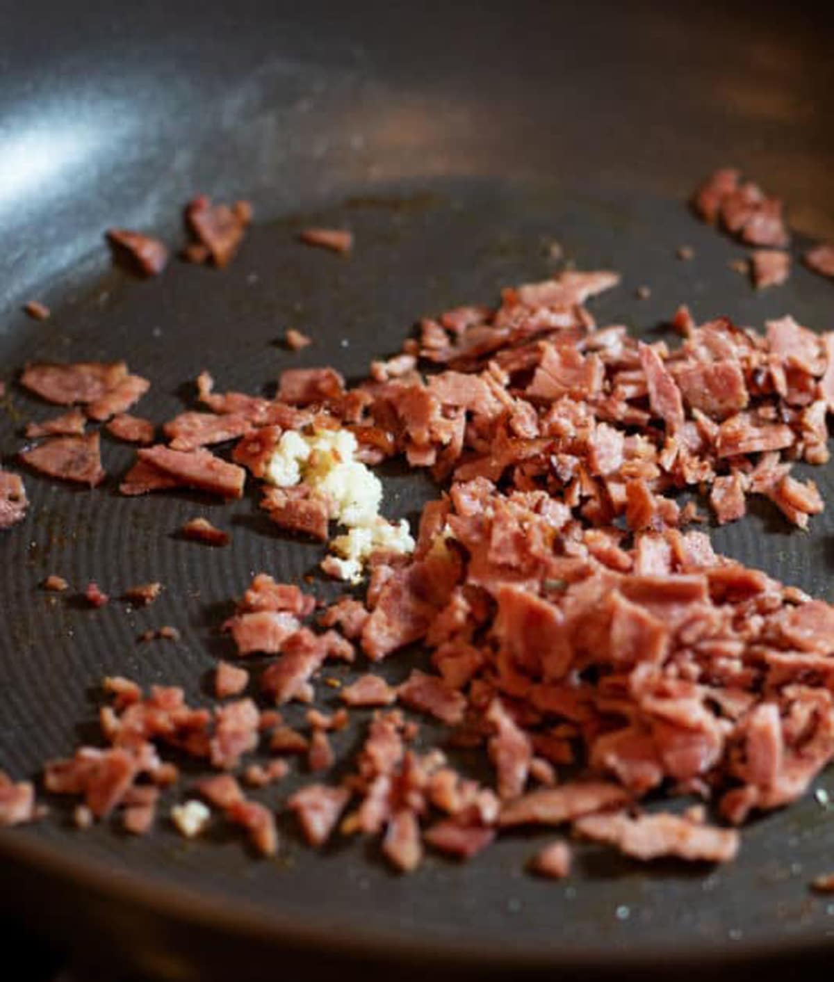 Turkey bacon and garlic being sauteed in a pan.