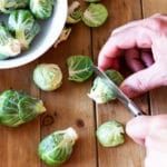 Person cutting the ends off Brussels Sprouts, brussels sprout leaves on table.