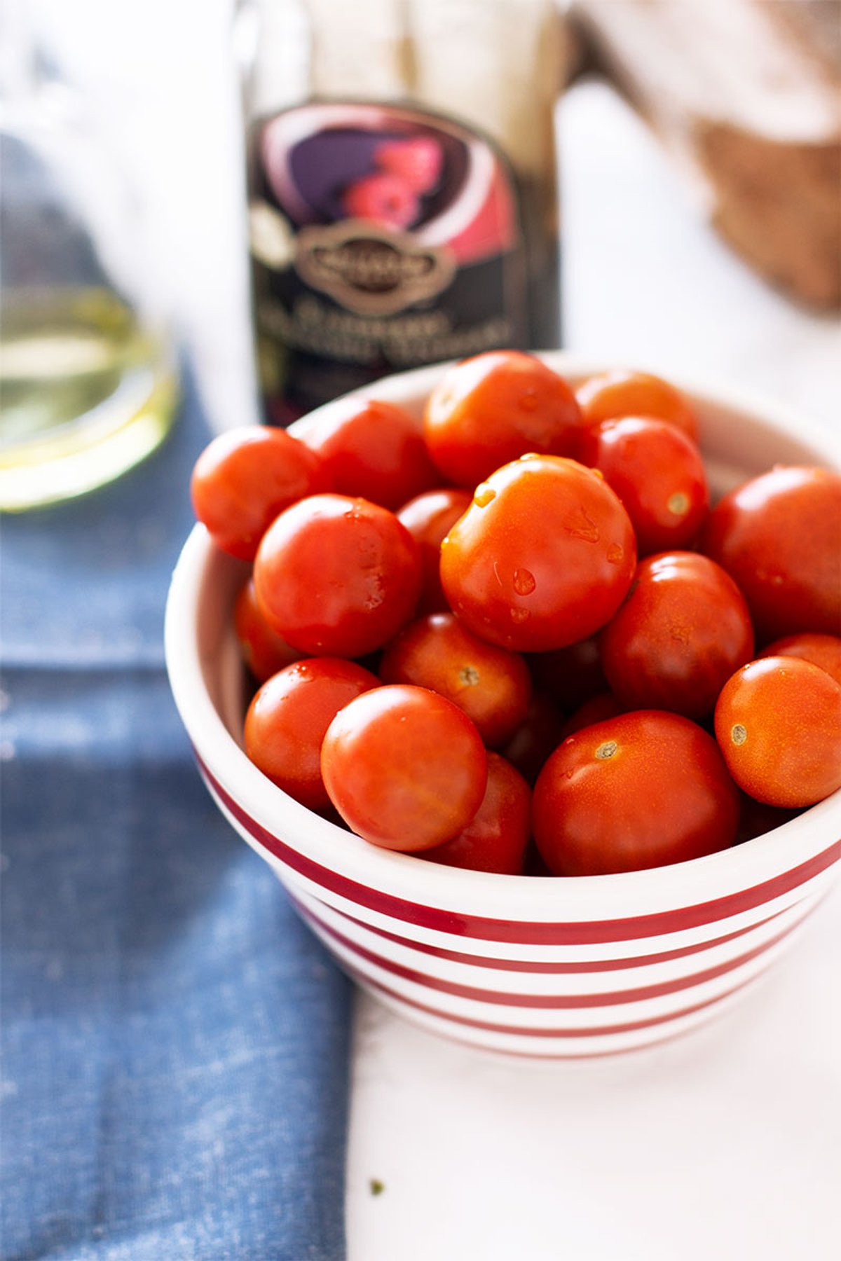 Red and white bowl containing cherry tomatoes sitting on a white table with a blue napkin.