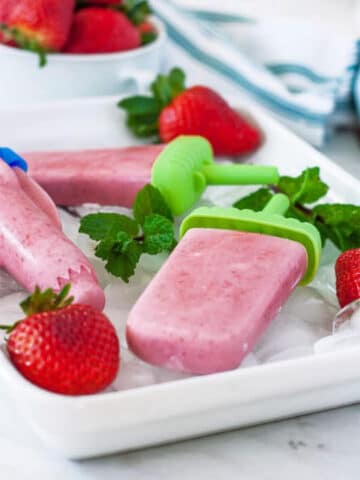 Strawberry popsicles in a tray of ice with mint and fresh strawberries.