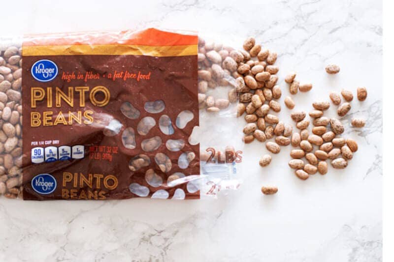 A bag of dry pinto beans spread out on a white marble table top.