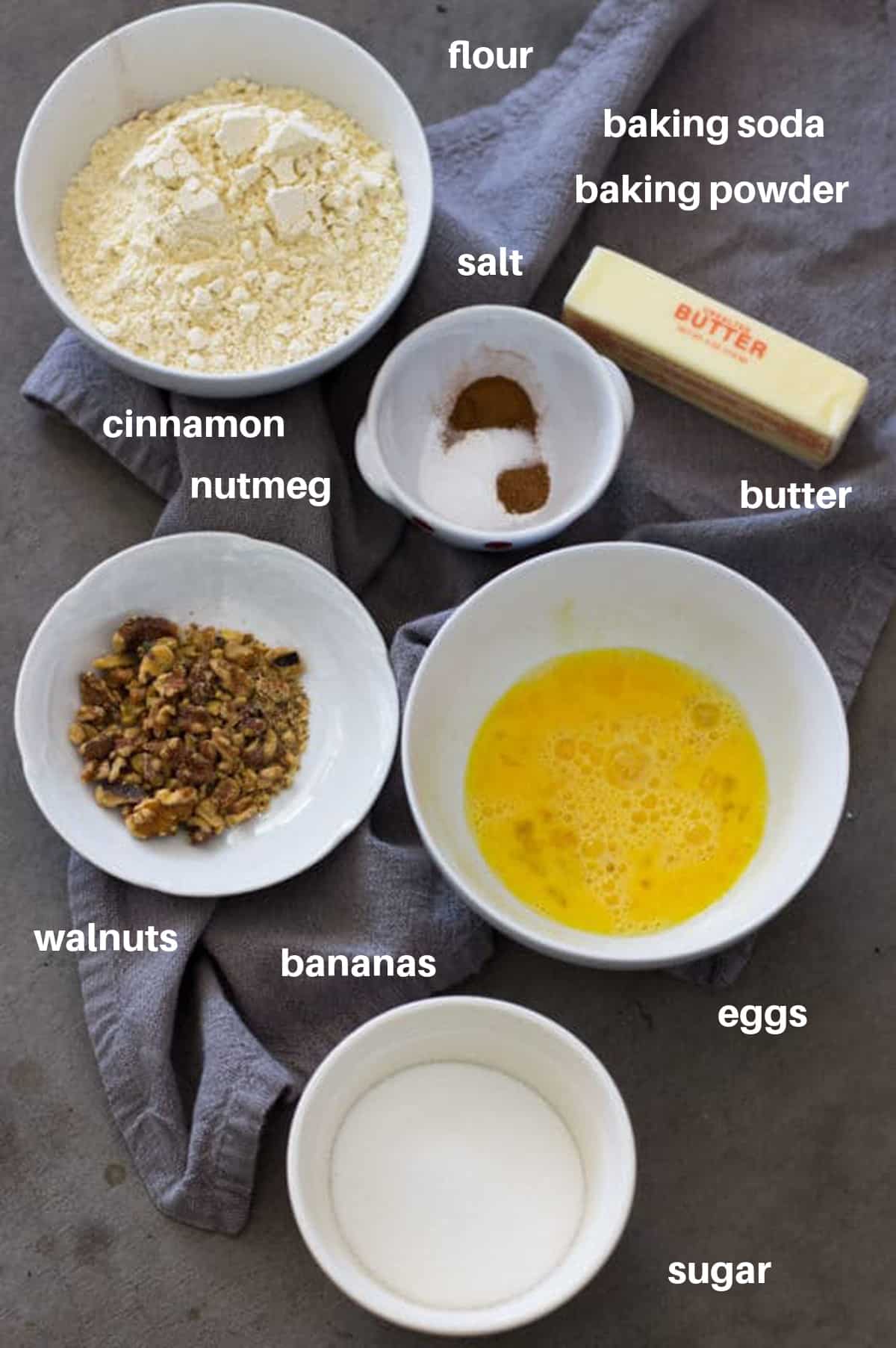 Ingredients to make banana bread, bowl of flour, eggs, butter, cinnamon, nutmeg, walnuts and sugar.