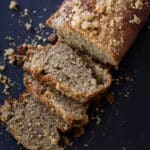 Sliced Banana Bread Loaf with Streusel-Nut Topping sitting on a black cutting board.