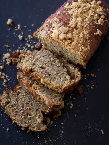 Sliced Banana Bread Loaf with Streusel-Nut Topping sitting on a black cutting board.
