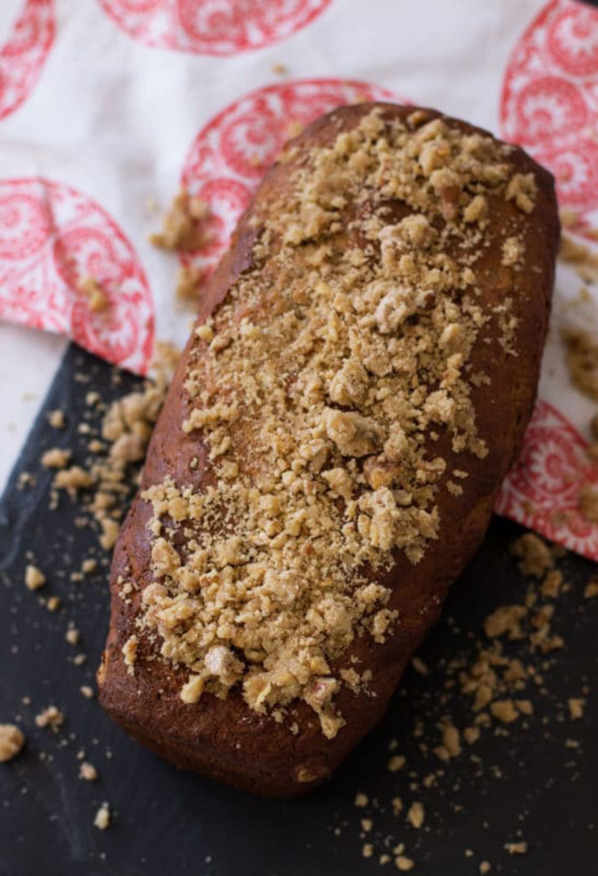 Loaf of Banana Bread with Streusel-Nut Topping sitting on a black cutting board.