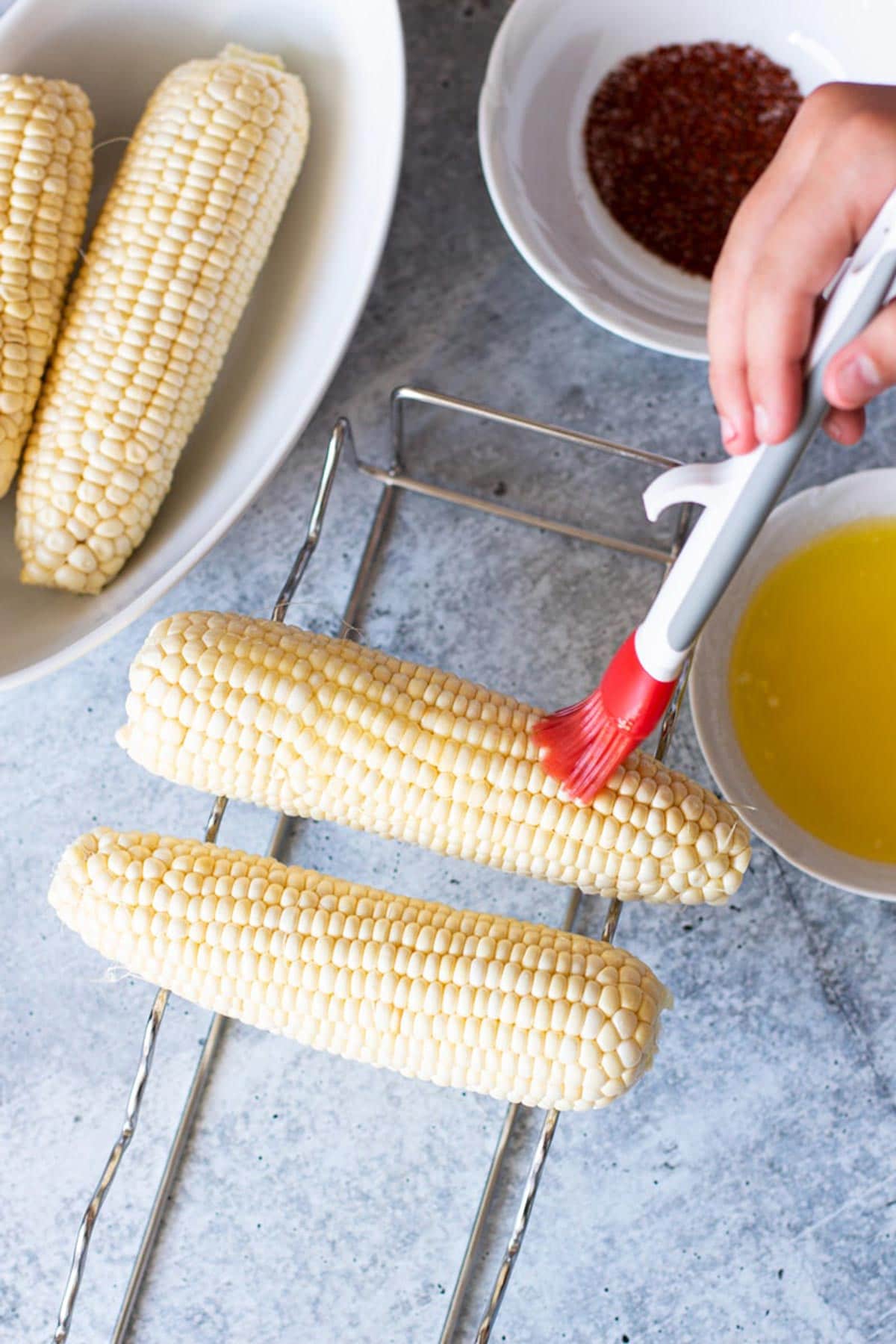 Person using basting brush to add butter to corn.