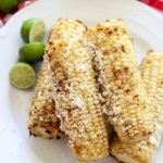 A close up of grilled corn on the cob covered with cotija cheese on a white plate.