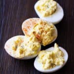 4 deviled eggs topped with paprika on a wooden table.