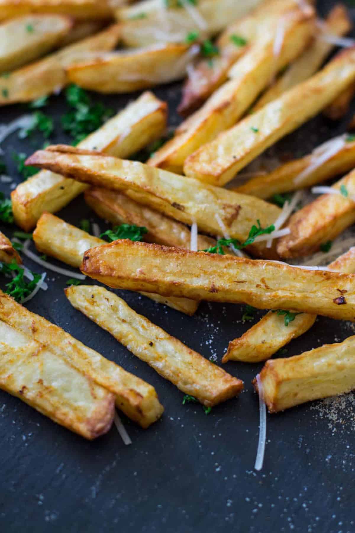 Close up of air fried french fries topped with seasoning salt, Parmesan cheese and parsley.