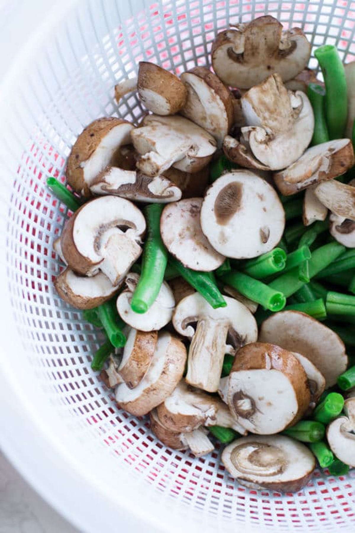 Sliced mushrooms and cut fresh green beans in a colander.