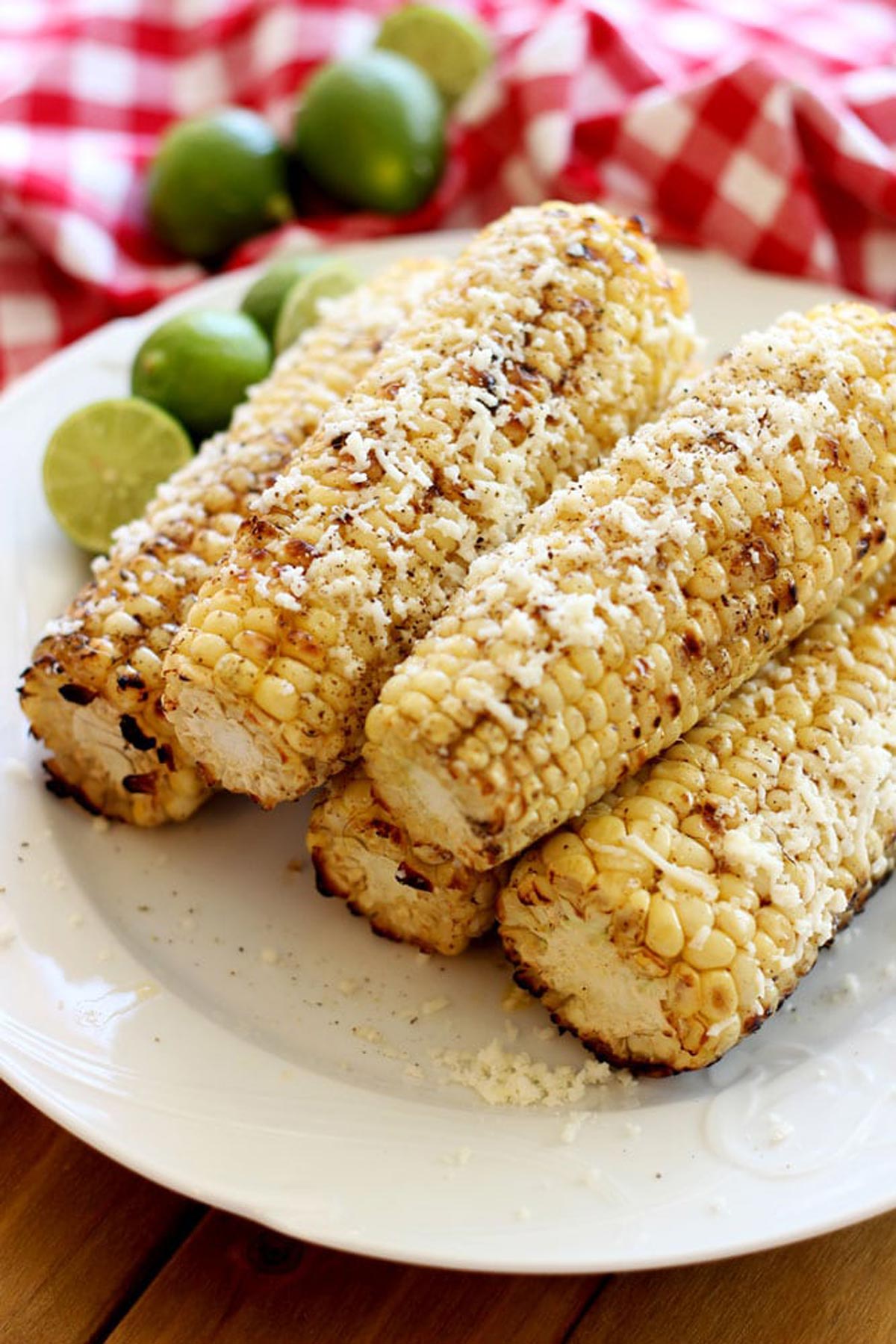 A plate of five grilled corn on the cobs covered with cotija cheese on a white plate.