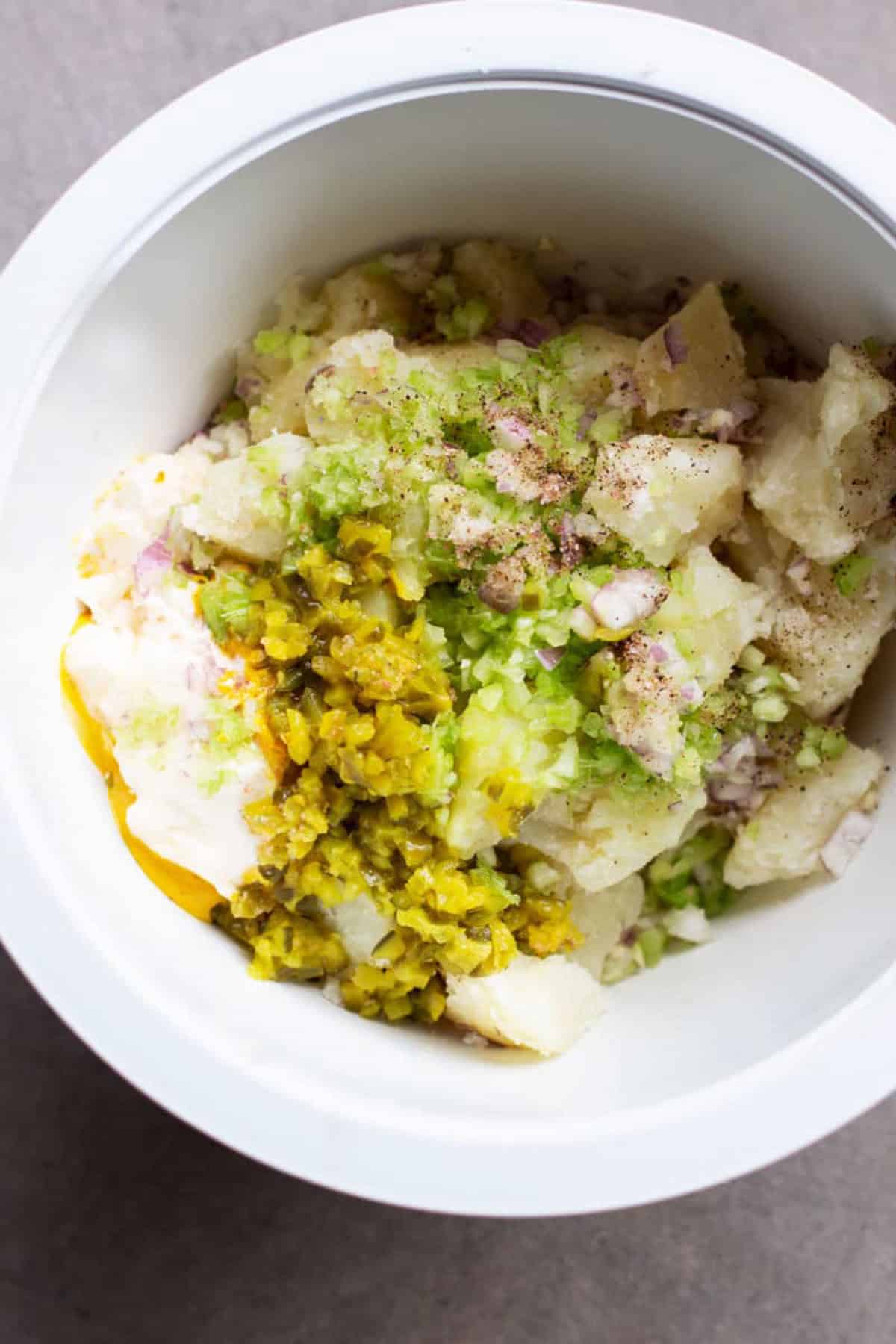 White bowl containing diced potatoes, celery, red onion, mustard, mayonnaise, and dill relish.
