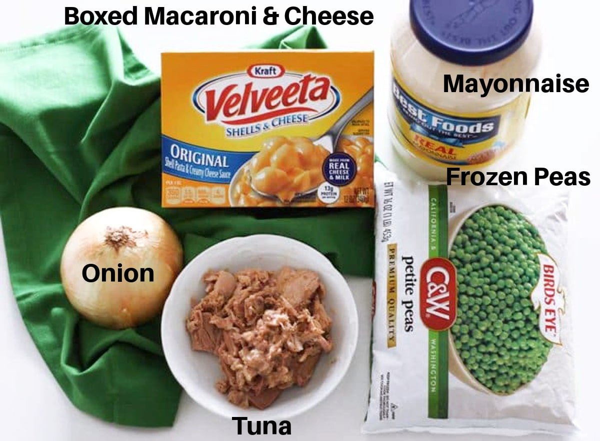 Onion, canned tuna, peas, Velveeta shells and cheese and a jar of mayonnaise sitting on a white background with a green napkin.