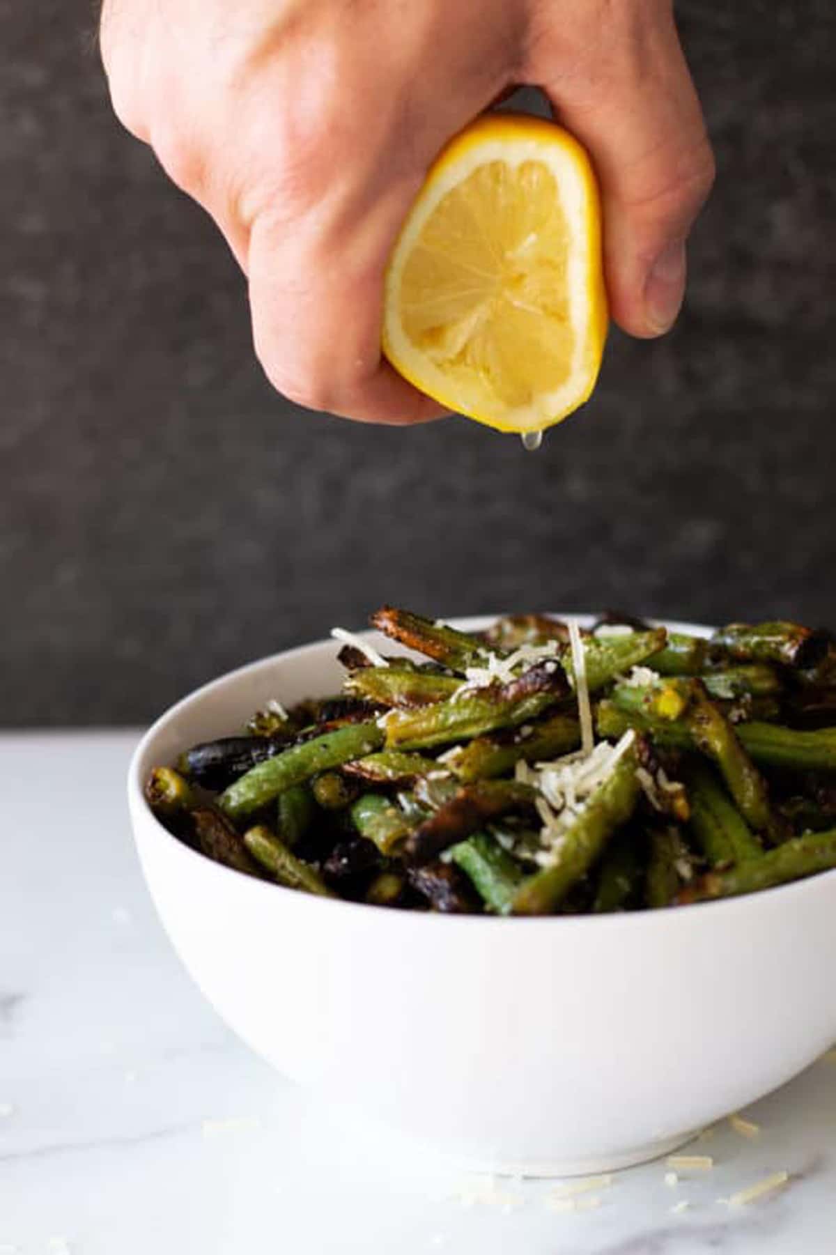 Fresh lemon being squeezed into a bowl of green beans. 