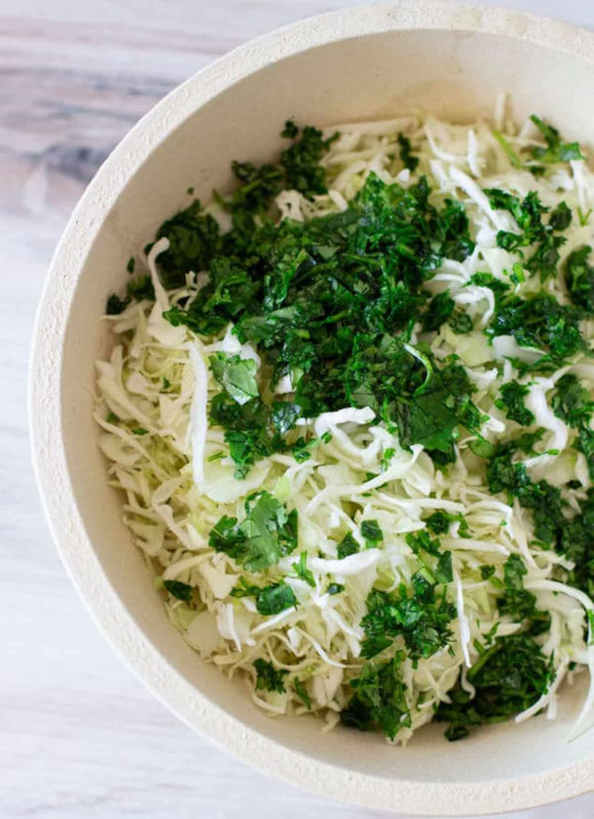 Bowl of slaw topped with chopped cilantro in a brown bowl.