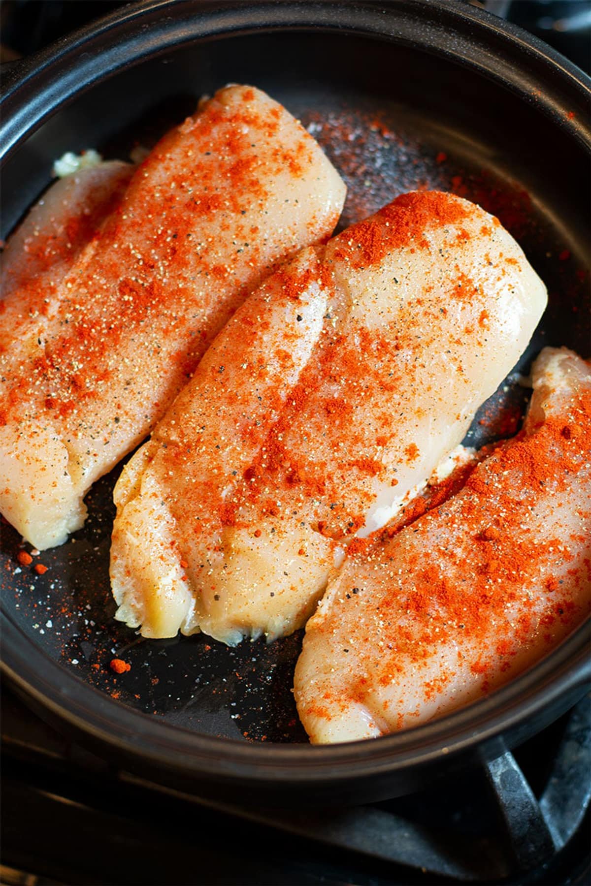 Three chicken breasts sprinkled with smoked Paprika, salt and pepper in a black pan.
