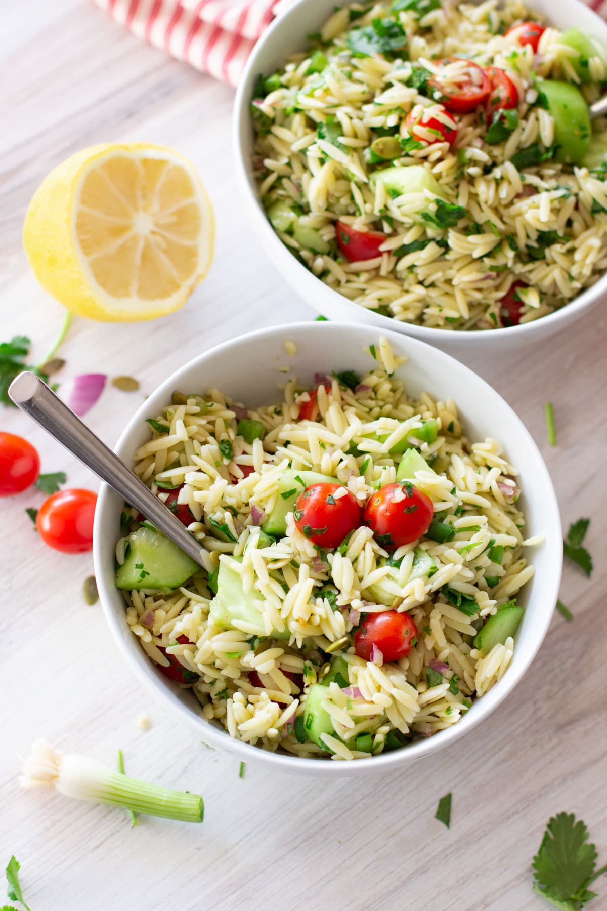 White bowl containing cooked orzo, cucumbers, cherry tomatoes.