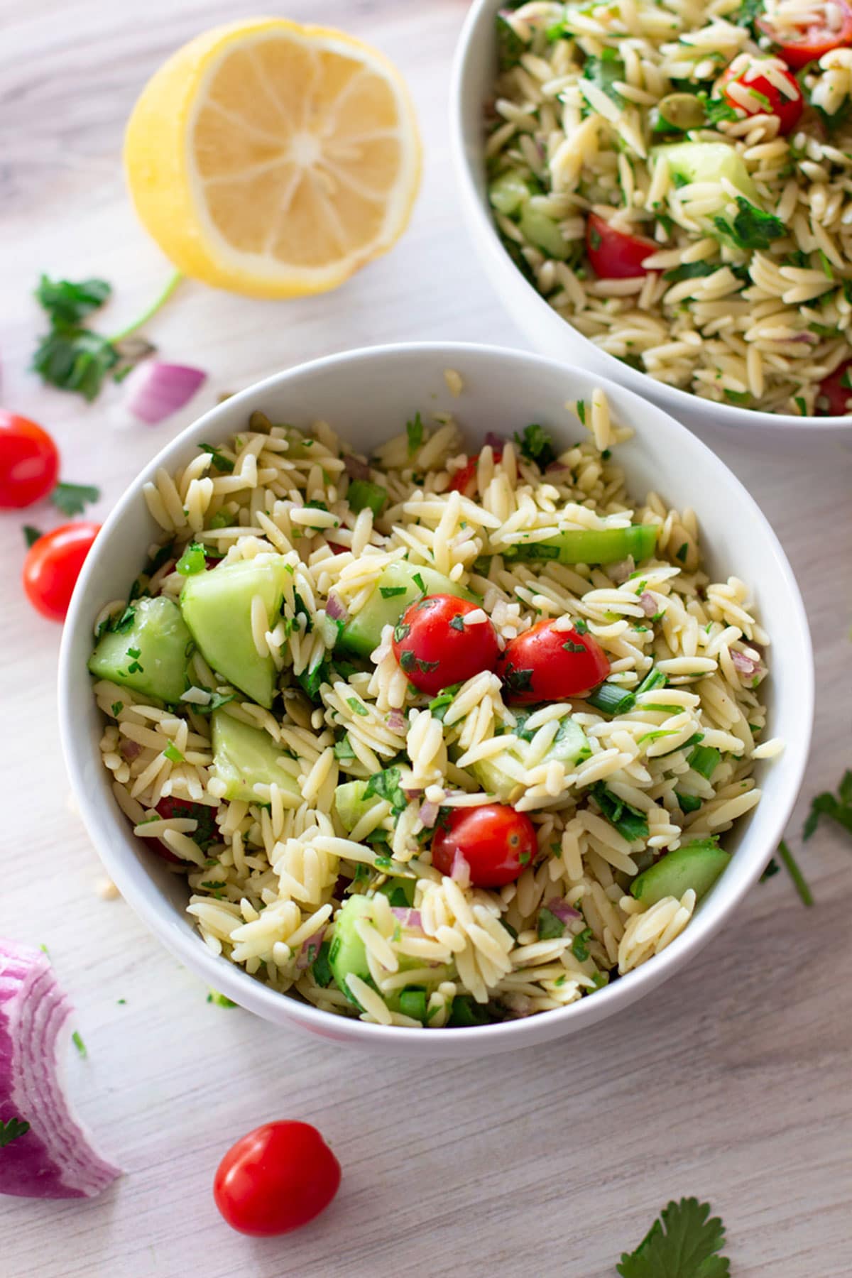 White bowl containing orzo salad with spoon in bowl.